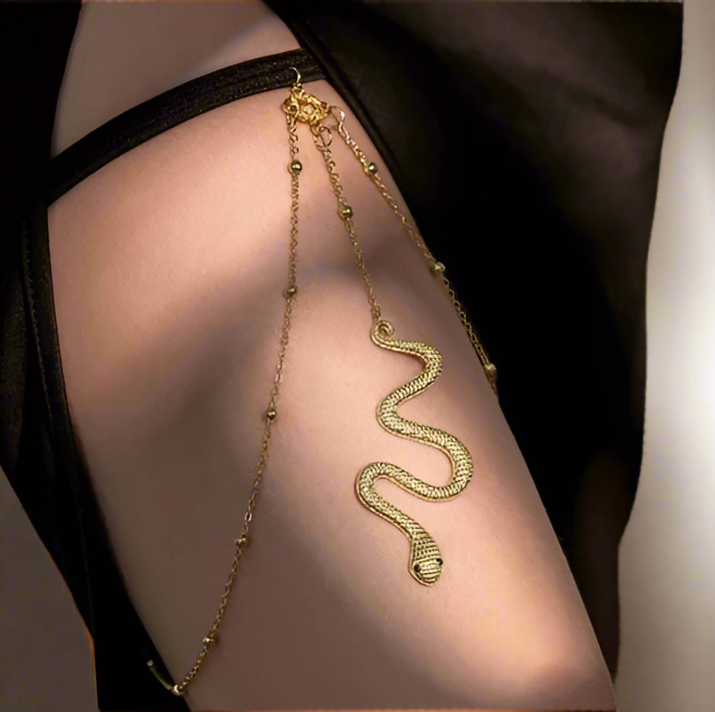 Gold snake-shaped leg chain on a woman's thigh against a neutral background