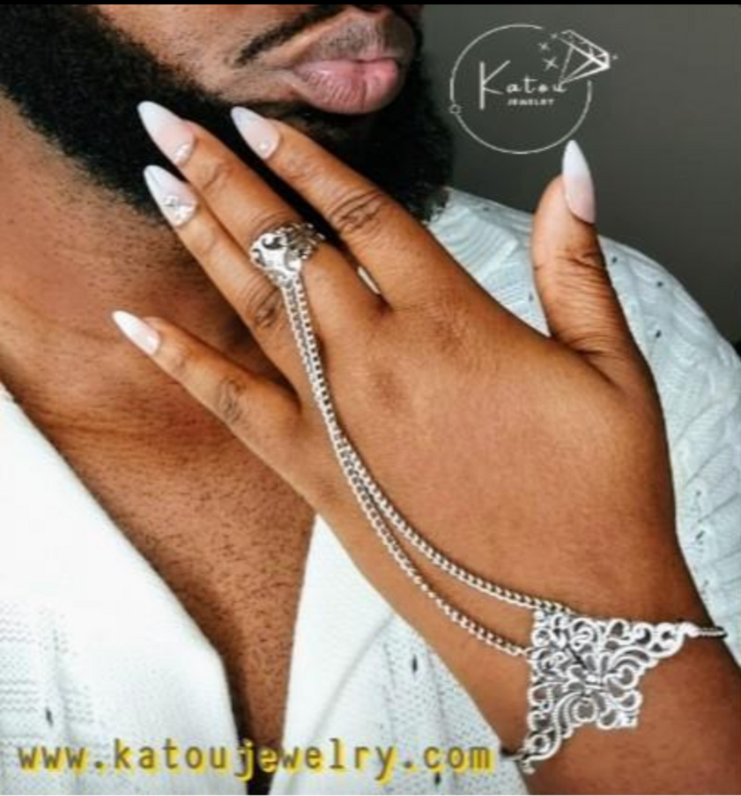 A person wearing a silver finger chain bracelet with intricate designs and small tassel details on the finger and forearm softly touching a gentleman's beard.