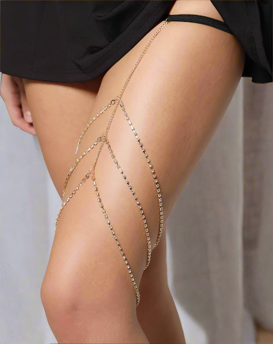 Gold chain leg accessory on a person's leg against a neutral background