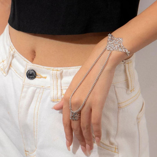 A woman wearing a silver finger chain bracelet with intricate designs and small tassel details on the finger and forearm.