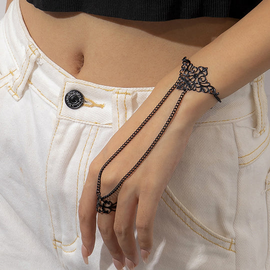 A woman wearing a black finger chain bracelet with intricate designs and small tassel details on the finger and forearm.