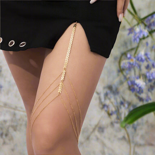 A close-up of a gold-colored wheat-shaped leg chain attached to a thigh, with a black skirt in the background.